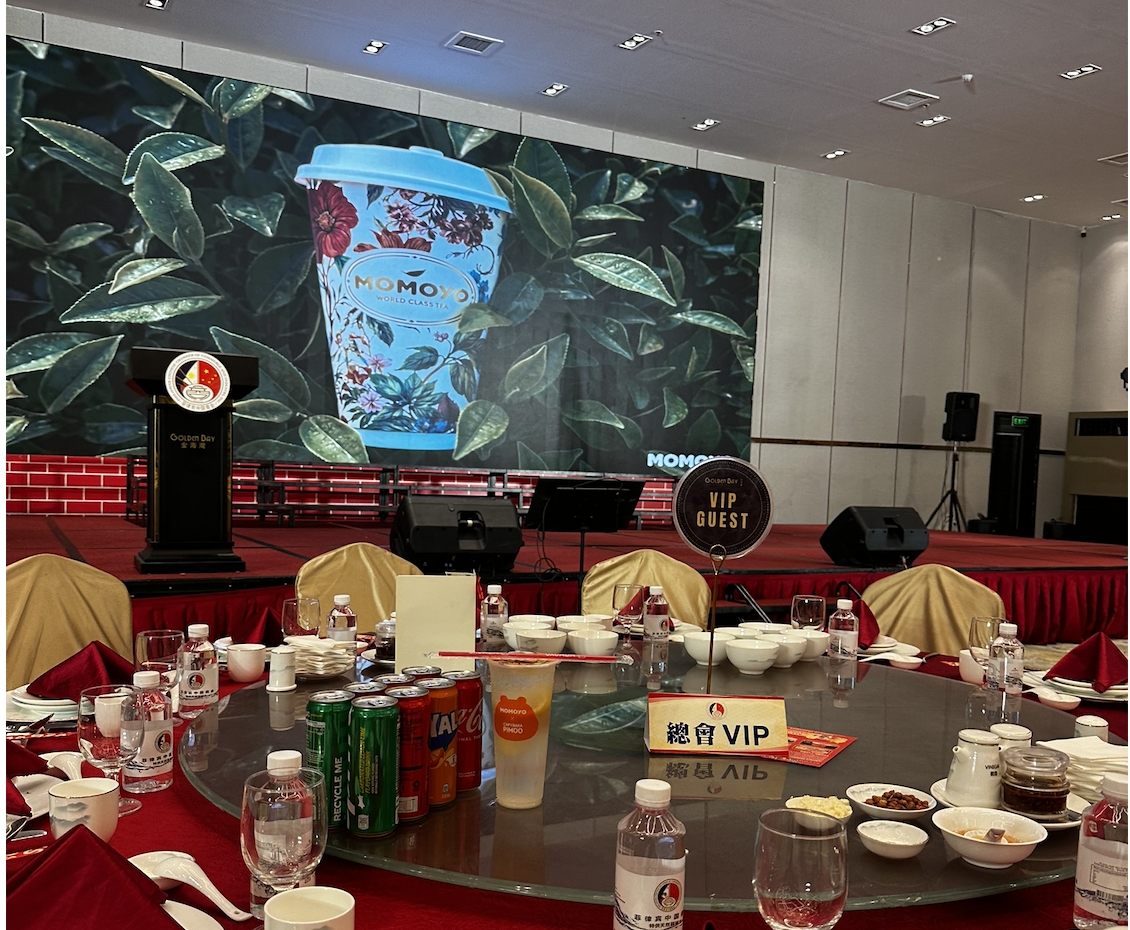 The MOMOYO brand video plays on the main screen of the hall